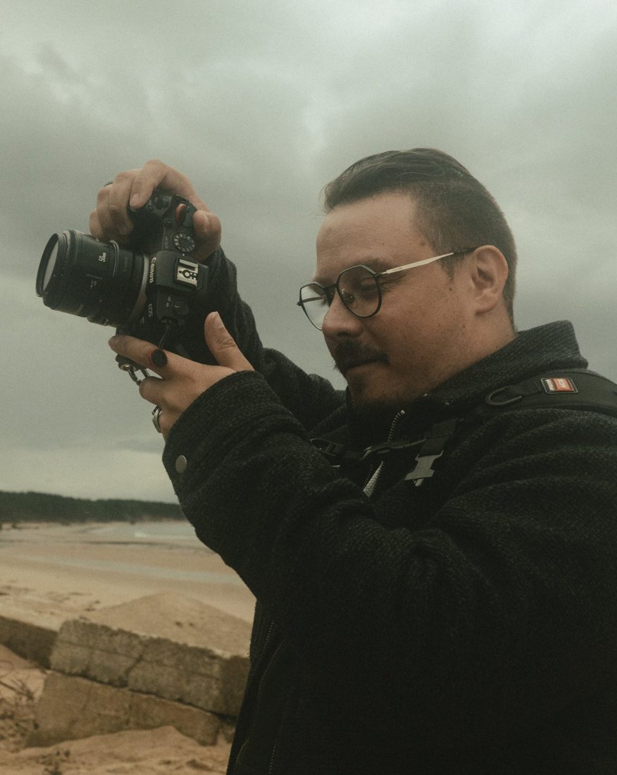 René mit Kamera am Strand unter grauem Himmel